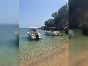 Two boats anchored in a serene cove with clear waters, while guests enjoy swimming nearby — a perfect summer getaway.