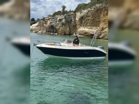 A sleek speedboat anchored in clear waters, showcasing its stylish design against a stunning rocky backdrop — perfect for day trips and water adventures.