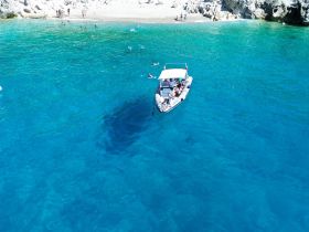 A vibrant scene of a group enjoying a day on the water, with a boat anchored near a beautiful beach and swimmers in the turquoise waters — perfect for summer adventures.