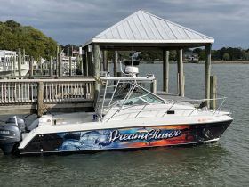 A sleek boat named 'Dream Chaser' docked at a marina, showcasing its vibrant design against a serene waterfront backdrop.