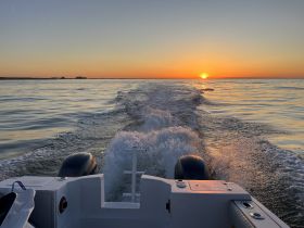 A stunning sunset view from the back of a boat, showcasing the tranquil waters and the wake trailing behind — perfect for evening cruises.