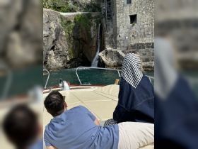 A couple relaxes on the deck of a boat, enjoying the scenic view of a waterfall cascading down rocky cliffs — a perfect moment for nature lovers.