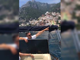 A man points towards the picturesque coastline while enjoying a boat ride, showcasing the stunning views of colorful houses nestled against the mountains.
