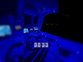 A sleek view of the helm inside a boat, illuminated in blue light at night, showcasing advanced navigation equipment and a modern design.