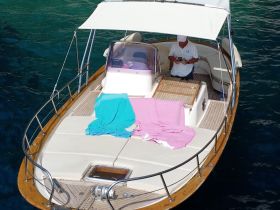 A serene view of the interior of a boat featuring a captain at the helm, with colorful towels laid out on the seating area, perfect for a relaxing day on the water.