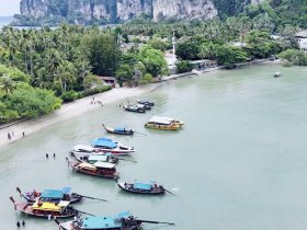 Aerial view of a vibrant beach scene with various boats anchored near the shore, showcasing a lively atmosphere with people enjoying the beautiful surroundings.
