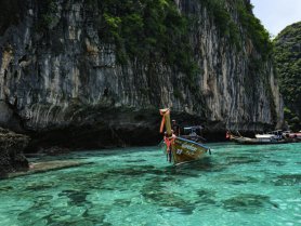 A traditional longtail boat navigates through crystal-clear waters near stunning limestone cliffs, showcasing the breathtaking scenery of a tropical paradise.