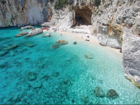 A stunning view of a secluded beach with crystal-clear waters, where visitors enjoy swimming and exploring the rocky coastline — a perfect destination for a day of adventure.