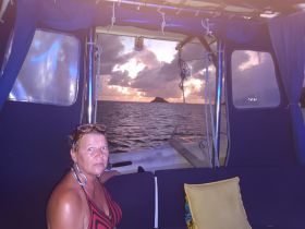 A woman relaxes inside the cabin of a boat, enjoying a stunning sunset view over the water — a perfect setting for a tranquil evening on the sea.