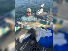 A proud angler displays a large snook caught while fishing on a boat, showcasing the thrill of a successful day on the water.