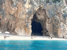 A stunning view of a beach with a cave backdrop, where visitors enjoy the sun and water activities — a perfect destination for adventure seekers.