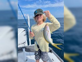 A young boy proudly holds up his catch while fishing on a boat, showcasing the excitement of a successful fishing trip.