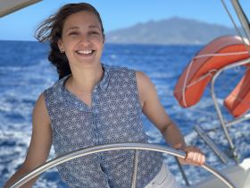 A woman enjoys a sunny day sailing on the ocean, showcasing the joy of boating adventures against a stunning backdrop.