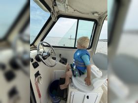 A young child sits at the helm of a boat, wearing a life jacket and enjoying the view — a perfect moment for family boating adventures.