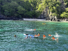 A lively group enjoys snorkeling and kayaking in crystal-clear waters near a secluded beach, perfect for adventure seekers and family outings.