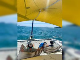 A family enjoys a relaxing moment on a catamaran, lounging on comfortable bean bags while taking in the beautiful ocean views — perfect for a day of leisure on the water.