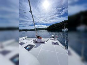 A person relaxes on the deck of a catamaran, enjoying the serene waters and lush surroundings — an ideal setting for a peaceful getaway.
