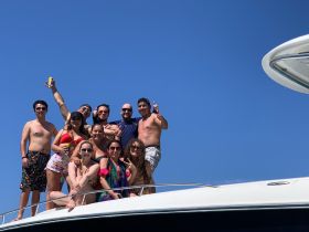 A lively group of friends celebrates on the deck of a yacht under a clear blue sky, capturing the essence of summer fun and camaraderie on the water.