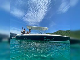 A couple enjoys a sunny day on their boat, striking playful poses against a backdrop of clear blue skies and turquoise waters — perfect for summer adventures.