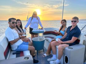 A group of friends enjoys a sunset meal on a pontoon boat, creating memorable moments against a stunning backdrop of the setting sun.