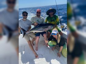 A group of friends proudly displays their catch of the day, a large tuna, while enjoying a fishing trip on the open water — a perfect moment for fishing enthusiasts.