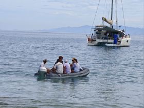 A group of guests enjoys a ride in a small boat while a catamaran is anchored nearby, showcasing a fun day on the water.