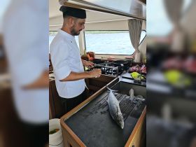 A chef prepares fresh fish in the kitchen of a boat, showcasing onboard culinary experiences and amenities for guests.