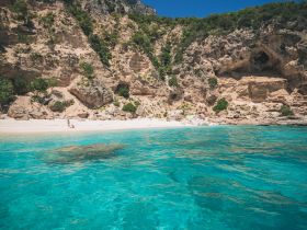 A stunning view of a secluded beach with crystal-clear turquoise waters and rocky cliffs, perfect for a relaxing day in nature.