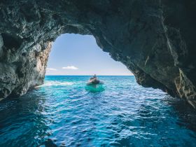 A boat navigates through a stunning cave entrance, showcasing the vibrant blue ocean beyond — an ideal scene for adventure seekers exploring coastal wonders.