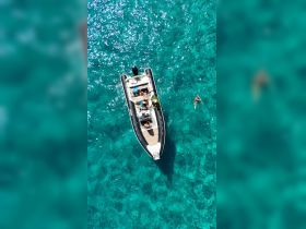 A lively group enjoys a day on the water aboard a boat, with one person swimming in the stunning turquoise waters — perfect for summer adventures and aquatic fun.