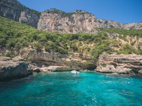 A scenic view of a small boat navigating through crystal-clear turquoise waters, surrounded by stunning cliffs and lush greenery — a perfect spot for exploration and adventure.