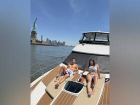 A couple enjoys sunbathing on the deck of a yacht with the iconic Statue of Liberty and New York City skyline in the background — a perfect day on the water.