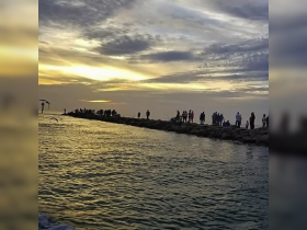 A vibrant sunset casts a warm glow over a crowd gathered on a jetty, creating a picturesque scene perfect for evening strolls and beach outings.