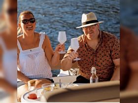 A couple raises their glasses in a toast while enjoying drinks on a boat, capturing a joyful moment perfect for celebrations on the water.