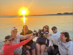 A joyful group of friends raises their drinks in celebration as the sun sets over the water, creating a perfect backdrop for memorable moments on the boat.