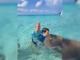 A child interacts closely with a stingray while swimming in crystal-clear waters, creating a memorable wildlife experience in the Bahamas.