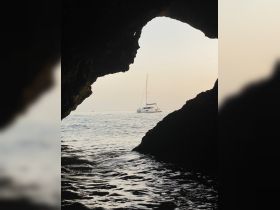 A serene view of a sailboat anchored off the coastline, framed by a natural rock arch, creating a picturesque scene perfect for coastal adventures.