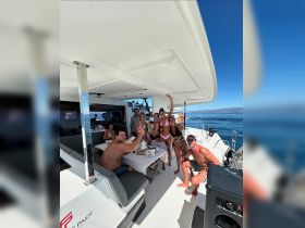 A lively group celebrates aboard a catamaran, enjoying food and drinks while soaking up the sun — perfect for unforgettable outings on the water.