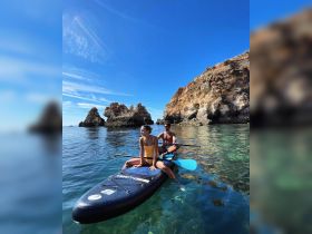 A couple enjoys paddleboarding in crystal-clear waters, surrounded by stunning rock formations — a perfect adventure for water enthusiasts.