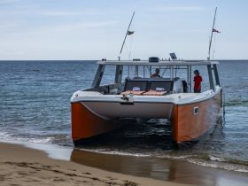 A vibrant catamaran approaches the beach with crew members on board, showcasing a perfect day for water adventures.