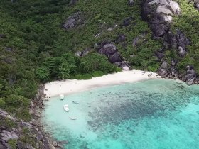 A stunning aerial view of a secluded beach surrounded by lush greenery and crystal-clear turquoise waters, perfect for island getaways and nature exploration.
