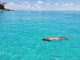 A child enjoys a serene moment floating in crystal-clear waters under a bright blue sky — a perfect snapshot of summer fun and relaxation.