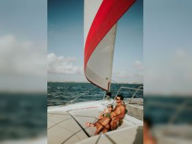 A couple enjoys a romantic moment aboard a catamaran, basking in the sun while sailing on clear waters — perfect for a getaway or special occasion.