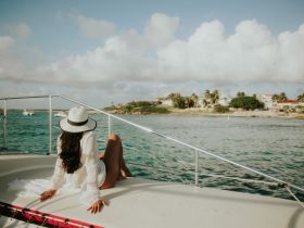 A woman relaxes on the deck of a yacht, enjoying the scenic view of the coastline and turquoise waters — a perfect moment for unwinding on a sunny day.