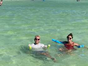 Two friends enjoy a fun day swimming in clear turquoise waters, equipped with colorful floatation devices — perfect for a relaxing beach outing.