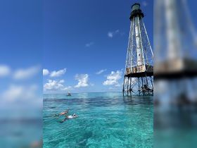 Two snorkelers explore the vibrant waters near a historic lighthouse, showcasing the beauty of marine life and clear blue skies — a perfect day for underwater adventures.