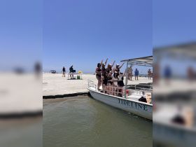A lively group of friends celebrates on a pontoon boat at the beach, capturing a fun moment in the sun — perfect for bachelorette parties or summer outings.