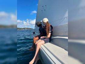 Two young girls enjoy a sailing adventure, sitting on the edge of the boat with their feet in the water — a perfect moment of fun and relaxation on the water.