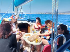 A lively group of friends enjoys drinks and snacks aboard a sailboat, celebrating together in the sun — perfect for a fun day on the water.