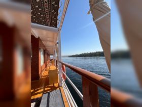 A serene view of the lounge area on a boat, showcasing wooden finishes and a beautiful riverside backdrop — perfect for relaxing while cruising.